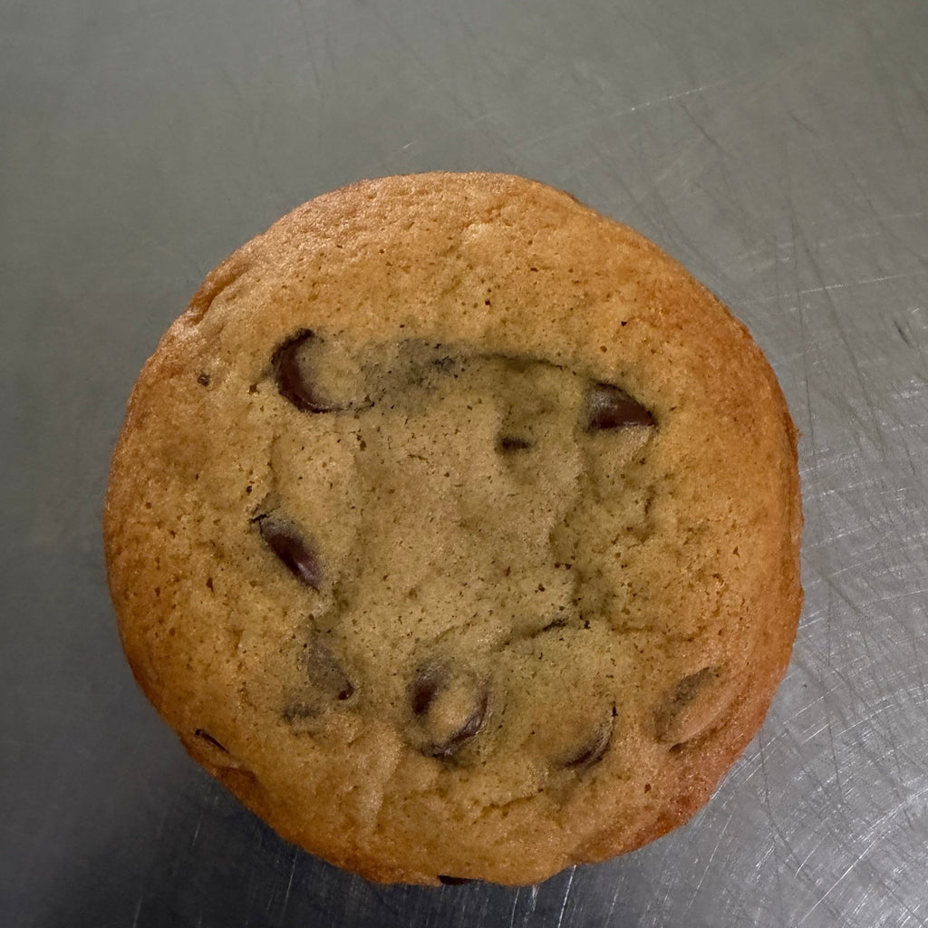SEBA Artisan Sourdough Chocolate Chip Cookie - Artisan Real Sourdough Bread Chef SebaArtisan Real Sourdough Bread Chef SebaArtisan Real Sourdough Bread Chef SebaSEBA-CCC-120A single chocolate chip muffin with golden-brown baked chips visible on top, photographed from above on a gray metal surface.