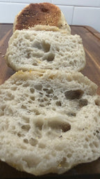 SEBAlicious™ Artisan Sourdough English Muffins Tuesday special - Artisan Real Sourdough Bread Chef SebaArtisan Real Sourdough Bread Chef SebaArtisan Real Sourdough Bread Chef SebaSEBA-EM-4-SD4 packSliced artisanal bread rolls showing a golden-brown crust and a soft, porous crumb, arranged on a wooden cutting board.