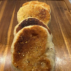 SEBAlicious™ Artisan Sourdough English Muffins Tuesday special - Artisan Real Sourdough Bread Chef SebaArtisan Real Sourdough Bread Chef SebaArtisan Real Sourdough Bread Chef SebaSEBA-EM-4-SD4 packThree golden-brown toasted flatbreads or pancakes sprinkled with herbs, stacked on a wooden cutting board with a white tiled wall in the background.