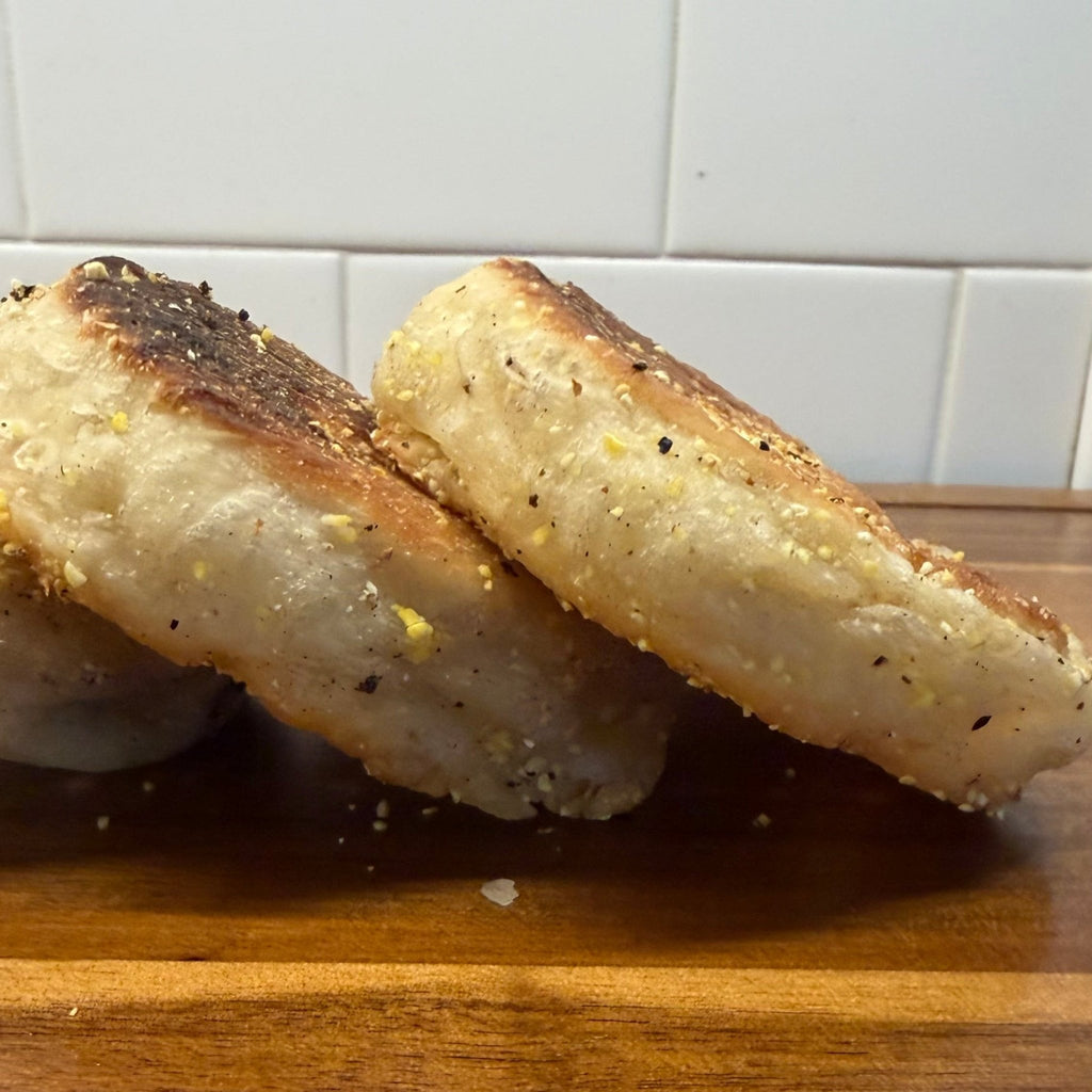 SEBAlicious™ Artisan Sourdough English Muffins Tuesday special - Artisan Real Sourdough Bread Chef SebaArtisan Real Sourdough Bread Chef SebaArtisan Real Sourdough Bread Chef SebaSEBA-EM-4-SD4 packThree slices of toasted English muffins with seasoning, stacked on a wooden cutting board with a white subway tile backsplash in the background.