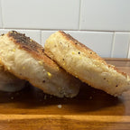 SEBAlicious™ Artisan Sourdough English Muffins Tuesday special - Artisan Real Sourdough Bread Chef SebaArtisan Real Sourdough Bread Chef SebaArtisan Real Sourdough Bread Chef SebaSEBA-EM-4-SD4 packThree slices of toasted English muffins with seasoning, stacked on a wooden cutting board with a white subway tile backsplash in the background.