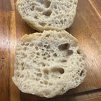 SEBAlicious™ Artisan Sourdough English Muffins Tuesday special - Artisan Real Sourdough Bread Chef SebaArtisan Real Sourdough Bread Chef SebaArtisan Real Sourdough Bread Chef SebaSEBA-EM-4-SD4 packTwo sliced round bread rolls with a golden-brown toasted top, showing a highly porous, airy crumb structure, resting on a wooden cutting board.