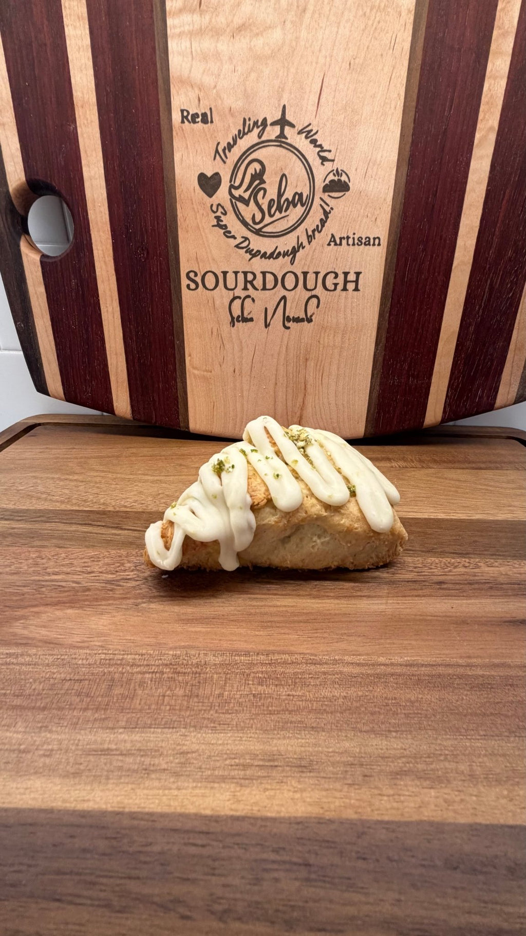 SEBAlicious™ Coconut Key Lime Pie Scones – Artisan Sourdough - Artisan Real Sourdough Bread Chef SebaArtisan Real Sourdough Bread Chef SebaArtisan Real Sourdough Bread Chef SebaSTRAW-SCONE-01singlePastry with white icing on a wooden cutting board with 'Lekan' branding.