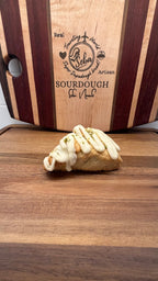SEBAlicious™ Coconut Key Lime Pie Scones – Artisan Sourdough - Artisan Real Sourdough Bread Chef SebaArtisan Real Sourdough Bread Chef SebaArtisan Real Sourdough Bread Chef SebaSTRAW-SCONE-01singlePastry with white icing on a wooden cutting board with 'Lekan' branding.
