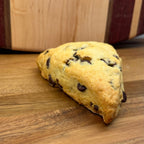 Sourdough Chocolate Chip Scones in Des Plaines, IL | Fresh Artisan Bakery by Chef SEBA - Artisan Real Sourdough Bread Chef SebaArtisan Real Sourdough Bread Chef SebaArtisan Real Sourdough Bread Chef SebaSTRAW-SCONE-01singleChocolate chip scone on a wooden surface with a wooden cutting board in the background