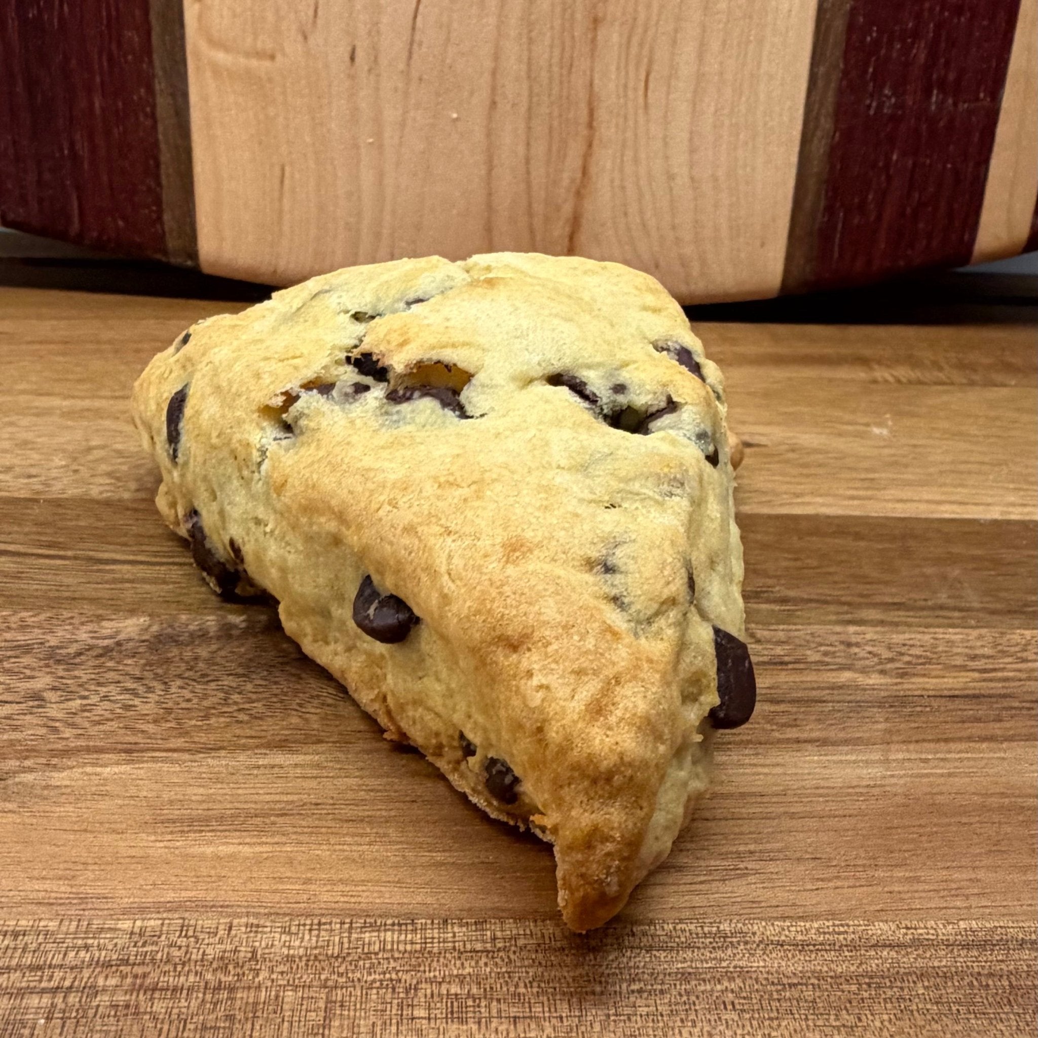 Sourdough Chocolate Chip Scones in Des Plaines, IL | Fresh Artisan Bakery by Chef SEBA - Artisan Real Sourdough Bread Chef SebaArtisan Real Sourdough Bread Chef SebaArtisan Real Sourdough Bread Chef SebaSTRAW-SCONE-01singleSour dough scone with chocolate chips on a wooden surface, branded 'Dempsey & Peabody'.